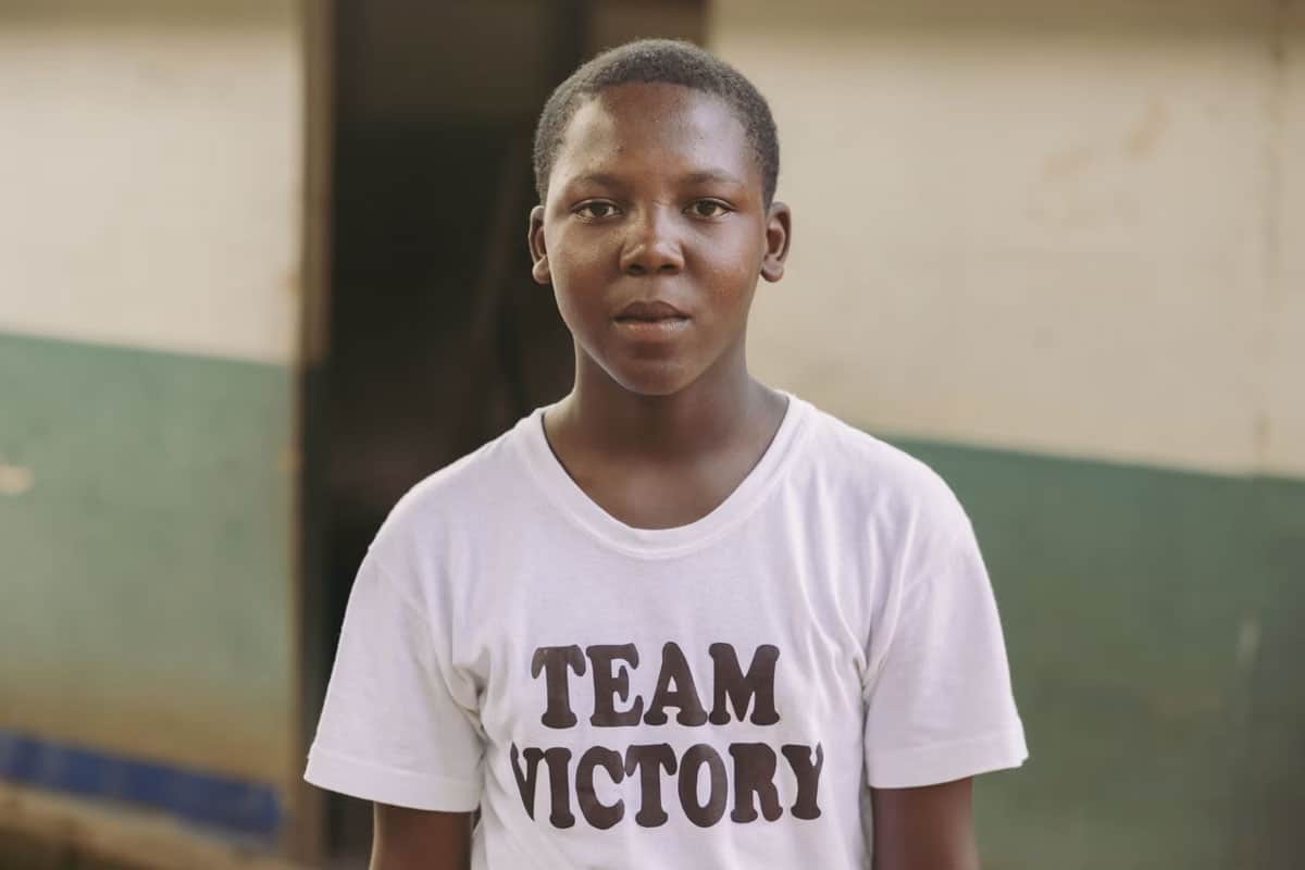 Haïti : Un jeune garçon regarde la caméra, vêtu d'un t-shirt blanc sur lequel on peut lire "Team Victory".