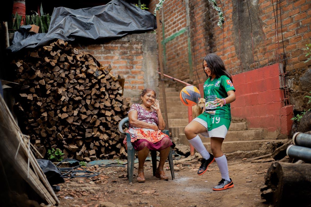 Karla, une enfant parrainée par Compassion, fait des dribles de football devant sa maison, sous les yeux de sa grand mère.